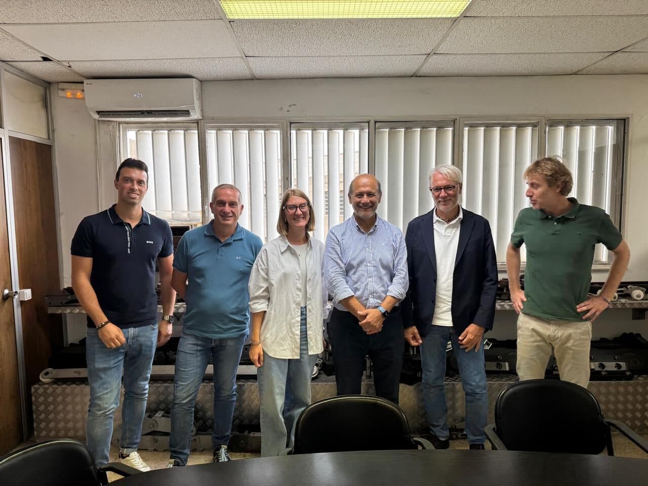 Seis personas posan en una sala de reuniones de Cadersa, con una muestra de componentes industriales al fondo, durante una visita a sus instalaciones en Ripollet, Barcelona, España
