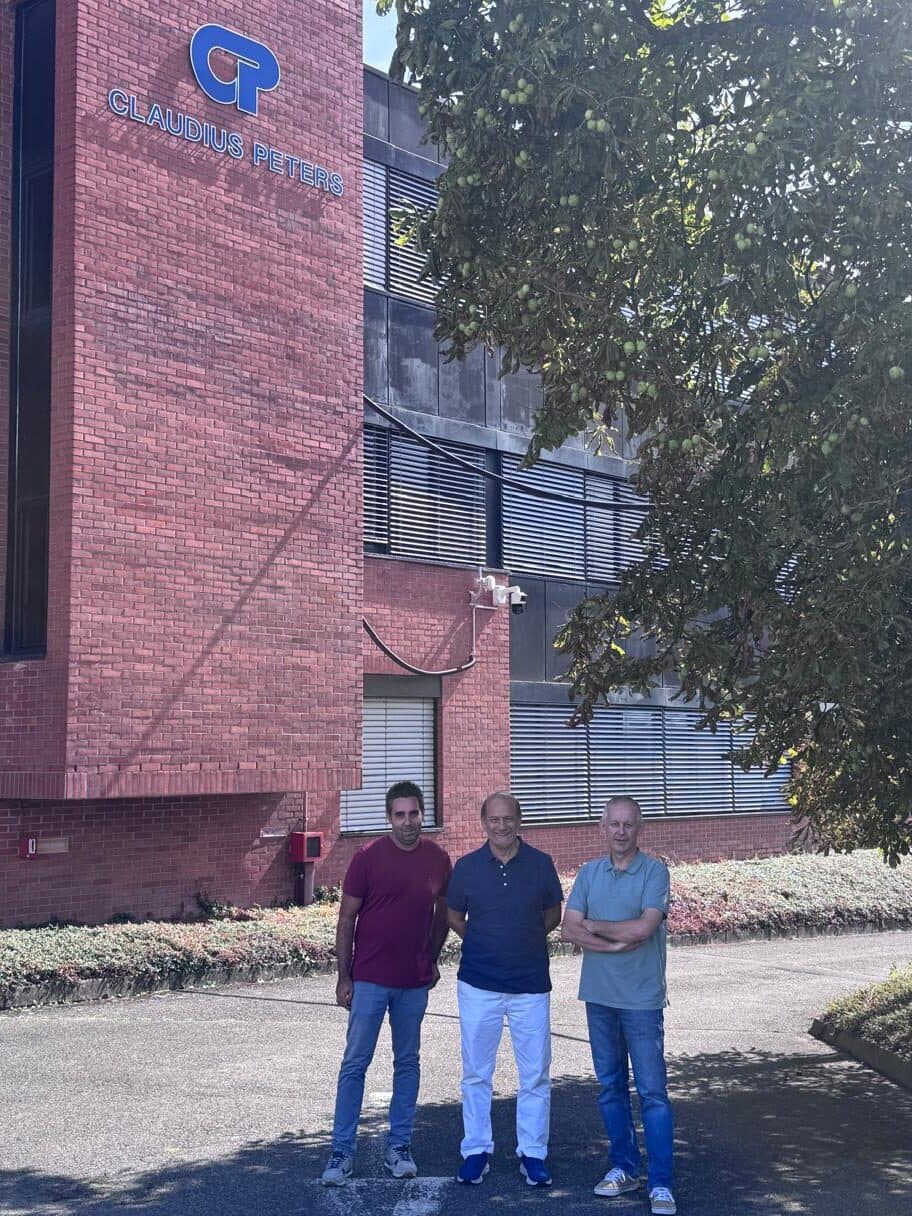 Tres personas posan frente al edificio de ladrillo de Claudius Peters, con el logotipo de la empresa en la fachada, durante una visita a sus instalaciones en Île Napoléon, Francia